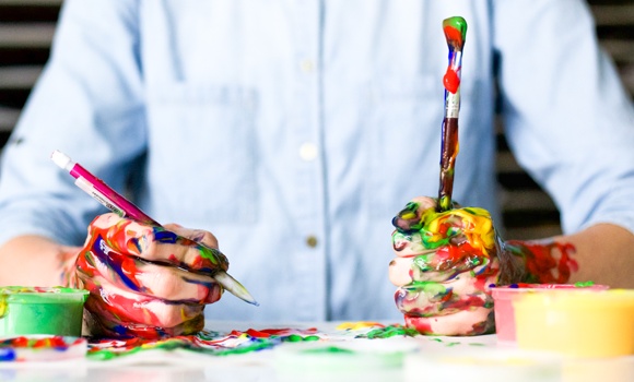 Personne avec des pinceaux dans les mains et les doigts recouverts de peinture